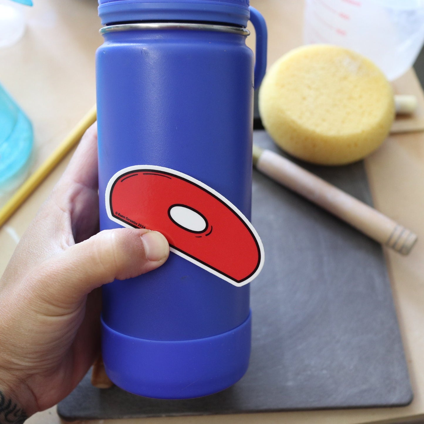 a red rubber pottery rib sticker held against a blue water bottle
